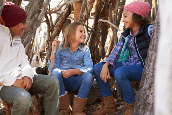 Three children sitting in a woodland den they’ve built.