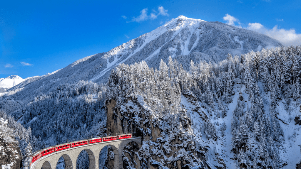 The Glacier Express in Switzerland passing over a viaduct in a snowy, mountainous landscape.