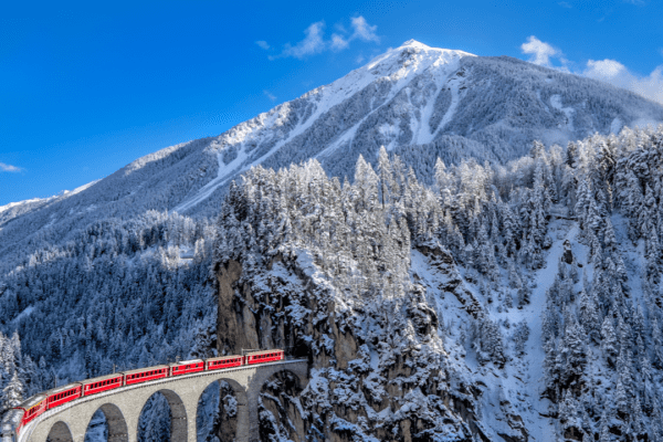 The Glacier Express in Switzerland passing over a viaduct in a snowy, mountainous landscape.